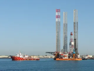 Offshore drilling rig positioned at the Abu Dhabi Corniche waterfront with an offshore supply vessel alongside